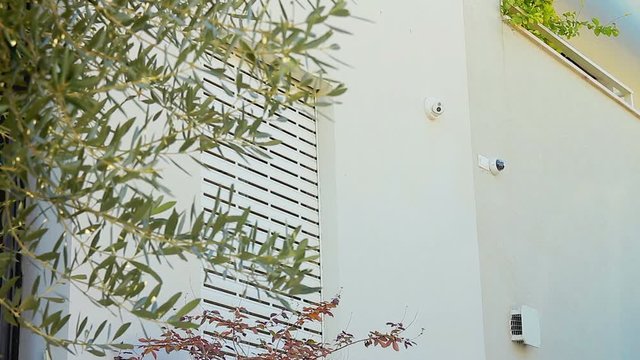 Outdoor smart home professional security cameras system. Electric rolling shutter opening on a window. Wide shot with a low angle.