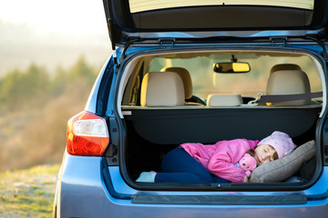 Pretty happy child girl sleeping with a pink toy teddy bear in a car trunk.