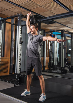 Athletic Man Performing Kettlebell Overhead Press At Gym