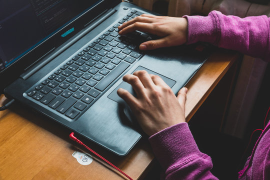 Young caucasian girl in pink sweater at computer while studying online programming at home near the window