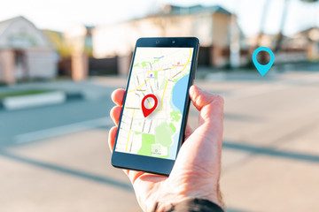 Male hand holding holding smartphone with online-card, which is a red icon of the location. In the...