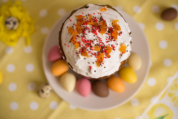 Fresh beautiful Easter cake on the plate with glaze and decorative egg candies on a yellow background, top view