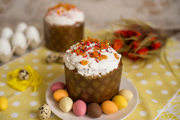 Fresh beautiful Easter cake on the plate with glaze and decorative egg candies and flowers on a bright yellow background