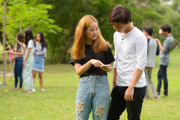 Fototapeta premium Young Asian couple using phone together with friends at the park