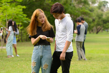 Fototapeta premium Young Asian couple using phone together with friends at the park