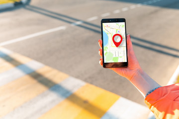 A woman's hand holds a smartphone with an online map that has a red geolocation icon. In the...