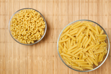 two bowls of dried pasta on a cane tablecloth