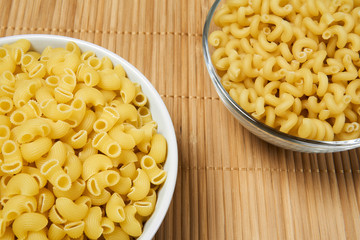 two bowls of dried pasta on a cane tablecloth, close-up