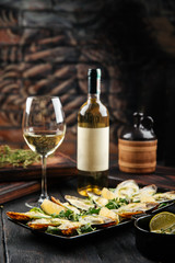 Side view on appetizing cooked oysters with sauce, bottle and glass of white wine, vertical