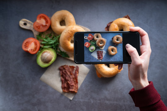 Woman taking a photo of salmon and bacon bagels with a mobile phone. Top view.