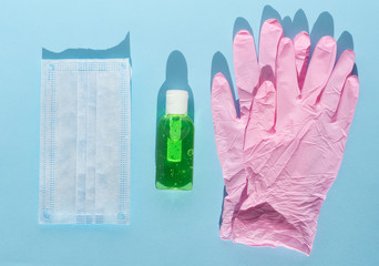 Sanitizer, pink rubber gloves and face medical protective mask on blue background. Flat lay, copy space, top view, shadow. Concept of disease, coronavirus, infection, hygiene, protection