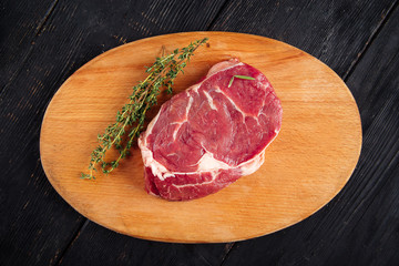 Top view on piece of fresh raw meat for cooking steak with sprigs of rosemary on a wooden board, horizontal
