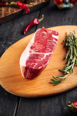 Top view on piece of fresh raw meat for cooking steak with sprigs of rosemary on a wooden board, vertical