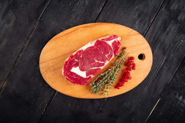 Top view on piece of fresh raw meat for cooking steak with sprigs of rosemary and currant on a wooden board, horizontal