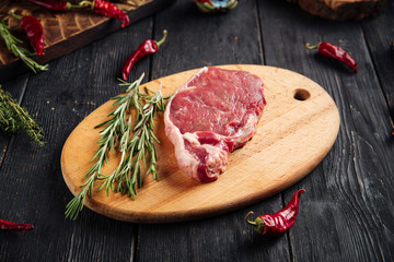 Side view on piece of fresh raw meat for cooking steak with sprigs of rosemary on a wooden board, horizontal