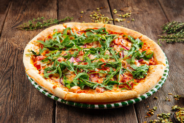 Side view on italian fresh cooked pizza with marinara sauce, red onion and arugula on the wooden table, horizontal format