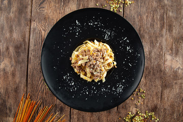 Top view on tagliatelle di almaz in a black plate on the wooden table, horizontal format