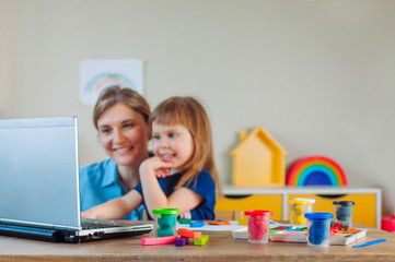 Smiling mother and toddler daughter molding colorful clay watching online learning lesson