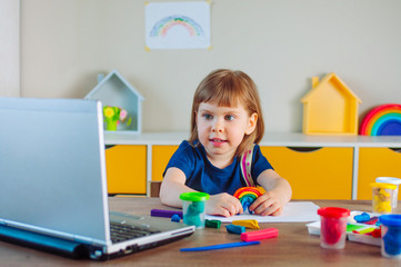 Smiling toddler girl molding colorful clay watching online learning lesson