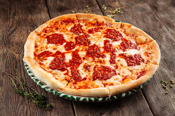 Closeup on hot cooked italian bolognese pizza with cheese and tomato marinara sauce, in a plate on the wooden table, horizontal format