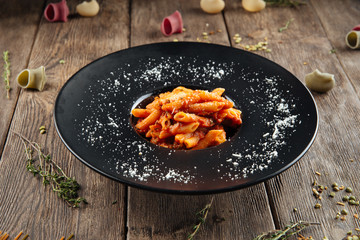 Side view on italian pasta penne arrabbiata with tomato sauce in a black plate on the wooden table, horizontal format