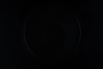 Empty black round plate with cutlery, knife and fork, on a black background. Top view