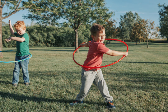 Two Funny Caucasian Preschool Boys Playing With Hoola Hoop In Park Outside. Kids Sport Activity. Lifestyle Happy Childhood Concept. Summer Seasonal Outdoor Game Fun For Kids Children.