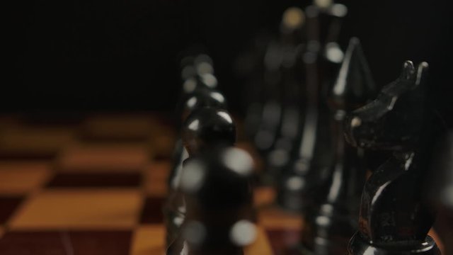 Black chess pieces on board. Camera tilting and refocusing from knight to king. Ready to hard brain game concept.