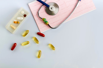 Stethoscope, cardiogram and pills and vitamins on a doctor’s table on a white background.