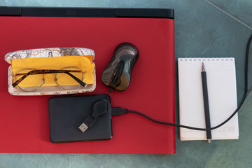 Glasses, external drive, mouse, notebook, red laptop