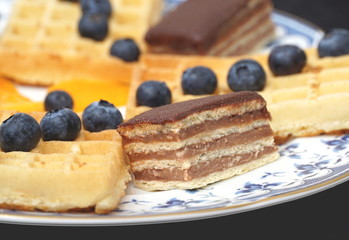 Sweet dessert on a plate. Homemade layer cake, waffles and blueberries close up