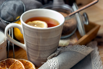 
A cup of black tea with lemon and spoon on a wooden table, next to a fresh lemon, sugar, closeup,...