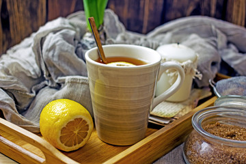 
A cup of black tea with lemon and spoon on a wooden table, next to a fresh lemon, sugar, closeup, copy space. Cozy background with a cup of tea and a slice of lemon
