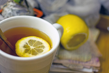 Hot black tea with a slice of lemon in a large gray mug with a spoon closeup, top view, next to dried oranges, fresh lemon, brown sugar, gray napkin on a wooden tray. The concept of a cozy home tea 