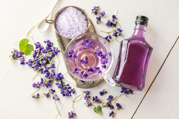 Cup of herbal violet violetta odorata tea with fresh spring blossom petals flowers on white  wooden...