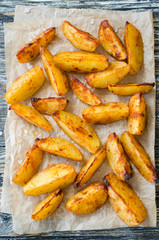 Golden spicy potato wedges fried or oven baked on wooden table.