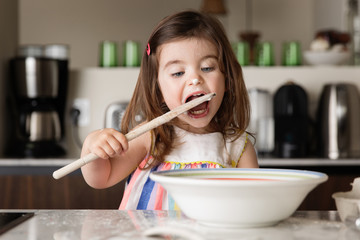 Cute toddler girl tasting food in kitchen