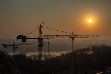 Sunrise over the city and the river. Sunrise over the construction. Silhouette of the city and construction cranes on a background of the sun.