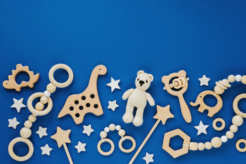 Cute wooden baby toys on blue background. Knitted bear, rainbow, dinosaur toy, beads and stars. Eco accessories,  beanbag and teethers for newborn. Flat lay, top view