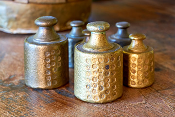Old copper or brass scale weights with calibration marks on wooden table in a bakery. Image with selective focus.