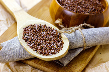 Brown raw dry flax seeds in a wooden spoon and bowl on a light background.