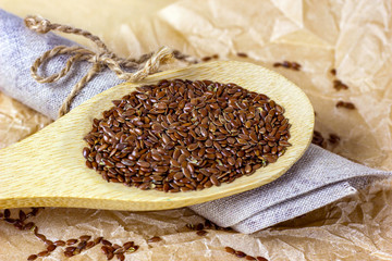 Brown raw dry flax seeds in a wooden spoon and bowl on a light background.