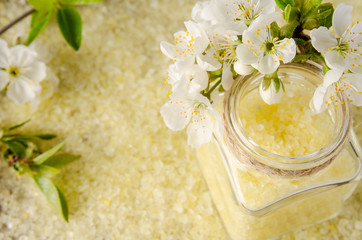 Obraz na płótnie Canvas Yellow bath salt crystals in glass bottle and cherry spring flowers with leaves as background for Spa or self care