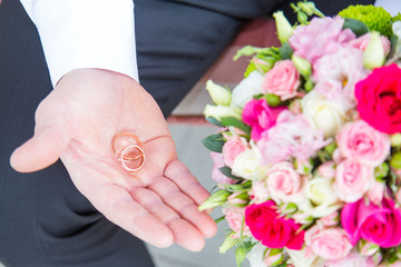 the groom holds in one hand two gold wedding rings and in the other hand holds a beautiful wedding bouquet of the bride