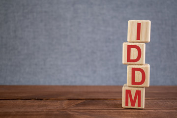 Abbreviation IDDM (insulin dependent diabetes mellitus) text acronym on wooden cubes on dark wooden backround. Medicine concept.