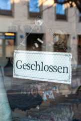 Schaufenster von Ladengeschäft mit Schild „Geschlossen“, in Deutsch, mit Auslagen und die Spiegelung der Umgebung in Unschärfe zur Zeit der Corona Covid-19 Pandemie im März 2020