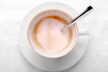 Empty half cup of latte or cappuccino coffee on white napkin, top view