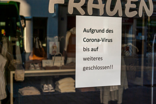 Schaufenster von Ladengeschäft mit Schild „Geschlossen wegen Corona-Virus“, in Deutsch, mit Auslagen und die Spiegelung der Umgebung in Unschärfe zur Zeit der Corona Covid-19 Pandemie im März 2020