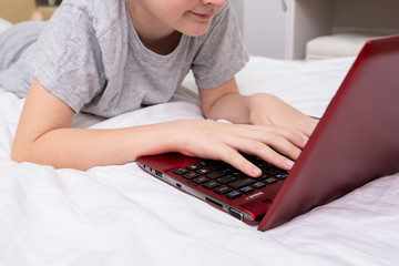 A boy, school boy lying in bed with a laptop and watching online translation, lesson, e-learning and education concept