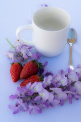 white cup with strawberries and purple flowers  on a table for breakfast